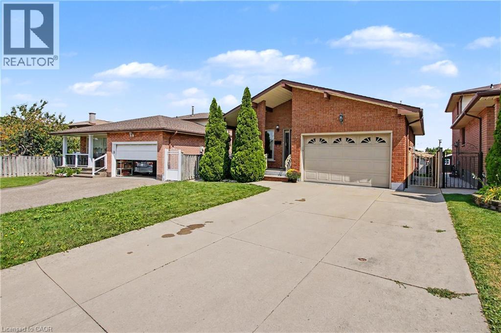 Brick exterior with an attached garage, paved driveway, and mature landscaping - 14 Indian Crescent, Hamilton, ON