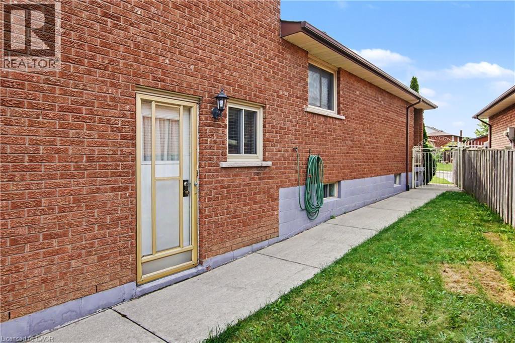 Red brick exterior with a light-colored storm door, featuring a wall-mounted exterior light fixture and a concrete walkway - 14 Indian Crescent, Hamilton, ON