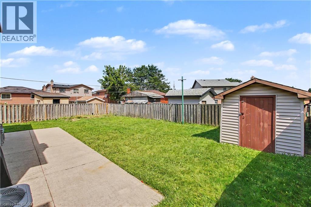 Expansive backyard featuring a concrete patio, grassy lawn, wood privacy fence, and a storage shed - 14 Indian Crescent, Hamilton, ON