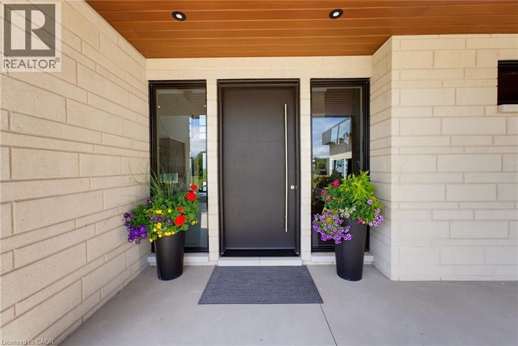 Welcoming entry featuring a dark-finish front door with sidelights, flanked by black planter vessels with seasonal flowers - 5709 Forth Line, Hillsburg, ON