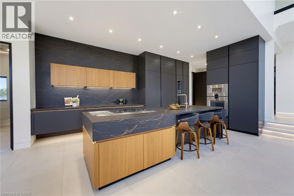 Contemporary kitchen featuring custom cabinetry in deep navy with natural wood-finish island, waterfall-edge countertop with dark stone finish, integrated stainless steel appliances, recessed ceiling - 5709 Forth Line, Hillsburg, ON