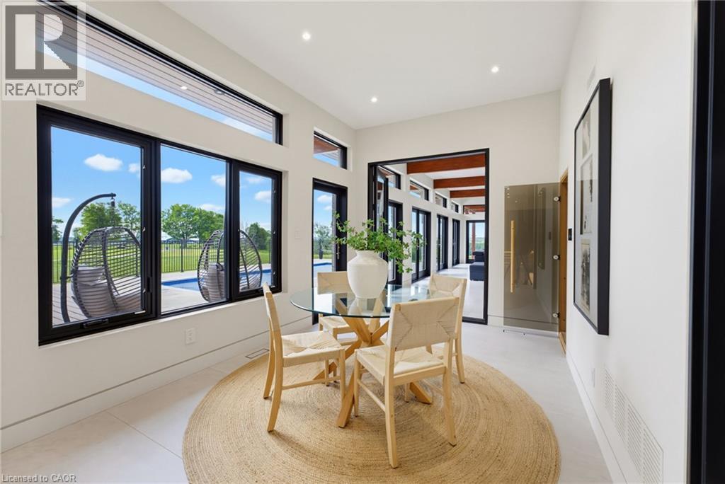 Bright dining area featuring floor-to-ceiling black-framed windows with expansive sightlines to the outdoor landscape, light wood-finish flooring, recessed ceiling lighting, and a circular jute area r - 5709 Forth Line, Hillsburg, ON