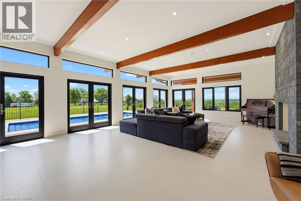 Spacious interior featuring a stone-clad fireplace, exposed wood beams, and an array of large windows and glass doors - 5709 Forth Line, Hillsburg, ON