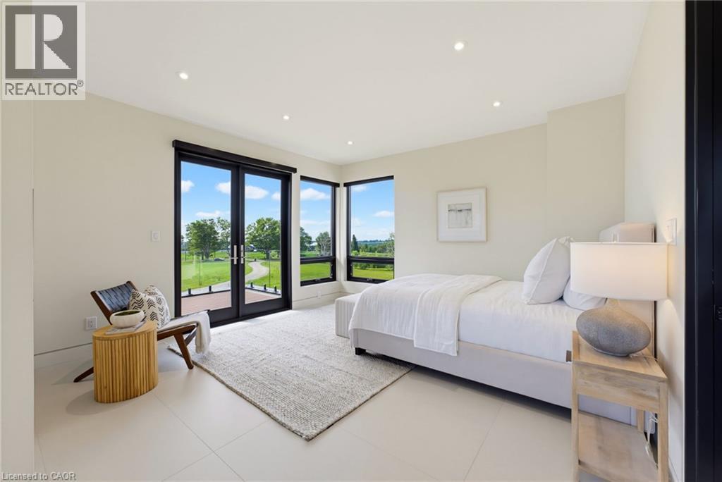 Bright, light-filled primary bedroom featuring floor-to-ceiling glass doors opening to manicured grounds, recessed ceiling lighting, neutral wall finishes, and polished concrete flooring throughout - 5709 Forth Line, Hillsburg, ON