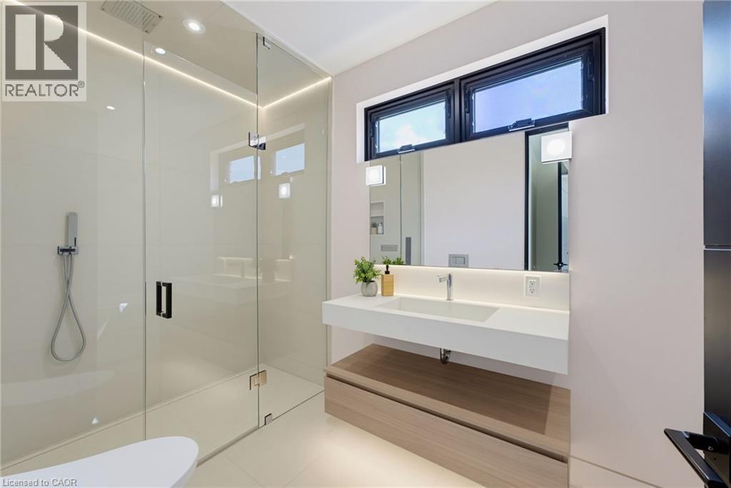 Modern primary bathroom featuring a frameless glass-enclosed walk-in shower with integrated rainfall showerhead, floating wood-finish vanity with an integrated rectangular sink and white quartz counte - 5709 Forth Line, Hillsburg, ON