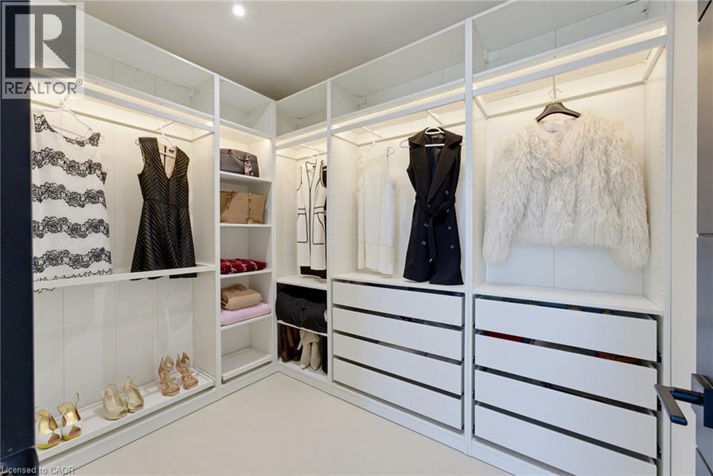 Custom walk-in closet featuring floor-to-ceiling glass-fronted cabinetry, built-in drawer storage with horizontal dividers, integrated hanging rods, recessed lighting throughout, and light wood-finish - 5709 Forth Line, Hillsburg, ON