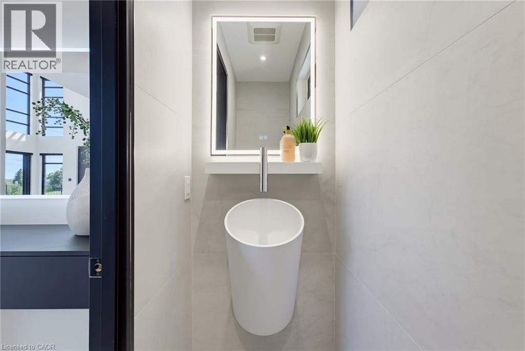 Modern powder room featuring a cylindrical vessel sink with polished chrome wall-mounted faucet, illuminated medicine cabinet with integrated LED mirror, neutral tile flooring, and clean minimalist de - 5709 Forth Line, Hillsburg, ON