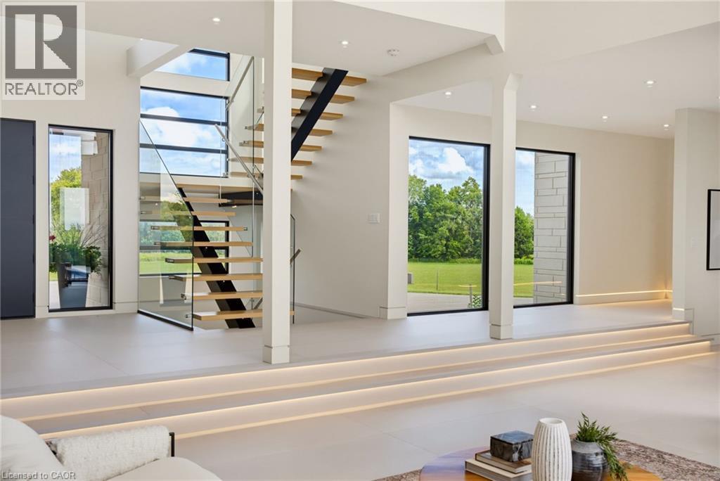 Open-concept living space featuring soaring ceilings with skylights, modern floating staircase with metal railings and wood treads, polished concrete flooring, and expansive glass sliding doors openin - 5709 Forth Line, Hillsburg, ON