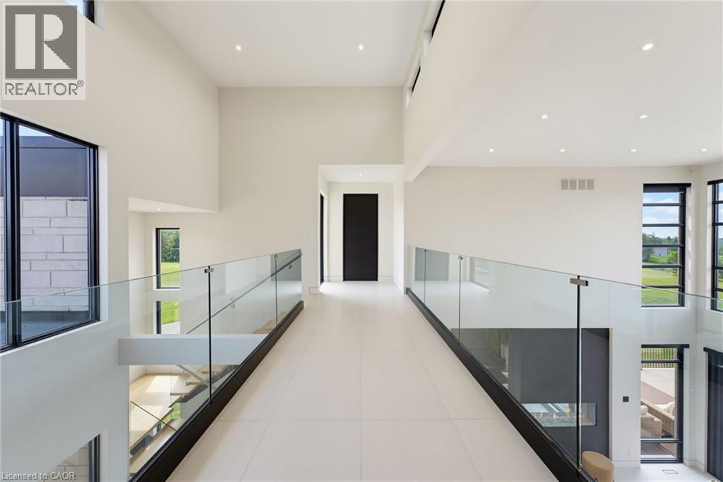 Modern hallway featuring polished concrete flooring, floor-to-ceiling white walls with recessed lighting, and glass railings with metal handrails flanking both sides - 5709 Forth Line, Hillsburg, ON