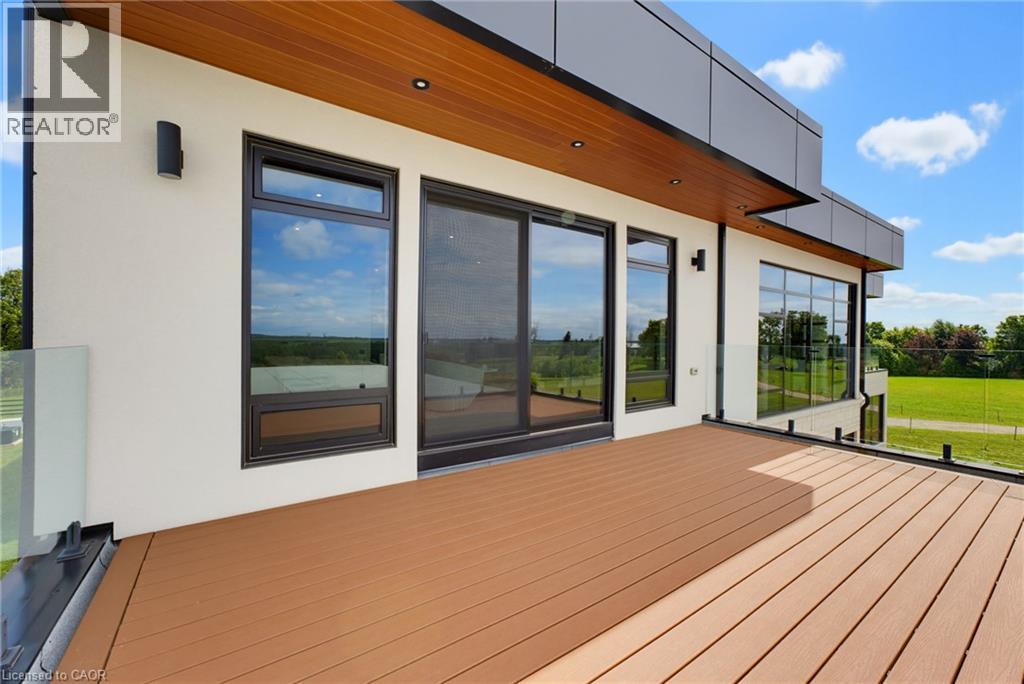 Spacious outdoor deck with wood-finish decking, glass panel railings, and modern black-framed windows - 5709 Forth Line, Hillsburg, ON