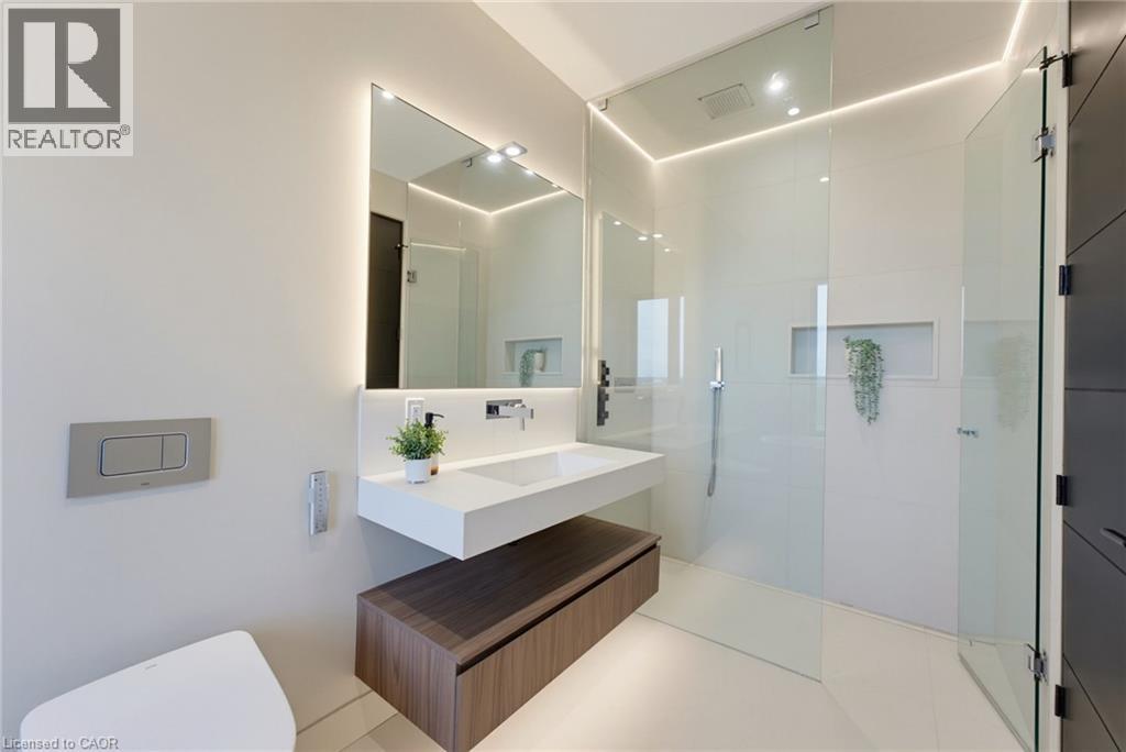 Modern primary bathroom featuring dual illuminated mirrors, a floating wood-finish vanity with integrated storage, white quartz countertop, frameless glass shower enclosure, and polished concrete floo - 5709 Forth Line, Hillsburg, ON