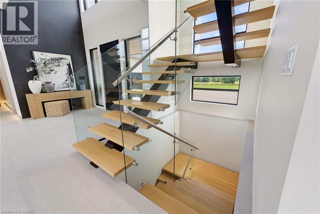 Modern staircase featuring floating wood-finish treads, sleek metal railings with glass panels, and a skylight above flooding the space with natural light - 5709 Forth Line, Hillsburg, ON