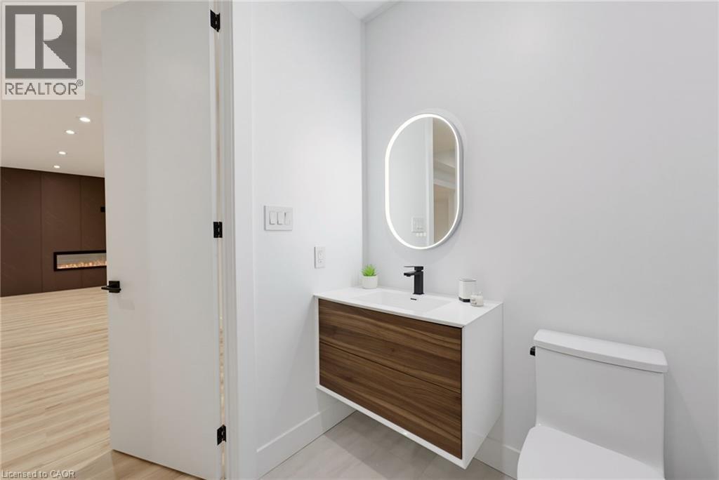 Modern bathroom featuring a wood-finish floating vanity with white countertop and integrated sink, matte black wall-mounted faucet, illuminated oval mirror with integrated lighting, and ceramic tile f - 5709 Forth Line, Hillsburg, ON