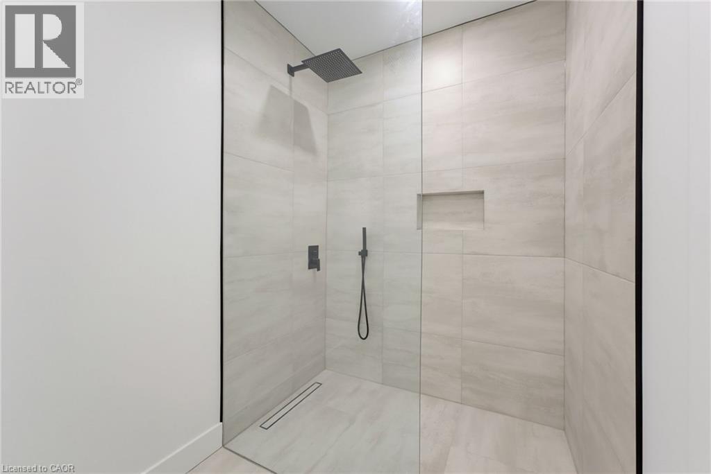 Walk-in shower with a glass enclosure, light-toned tilework, a built-in shower niche, a linear drain, and matte black fixtures - 5709 Forth Line, Hillsburg, ON