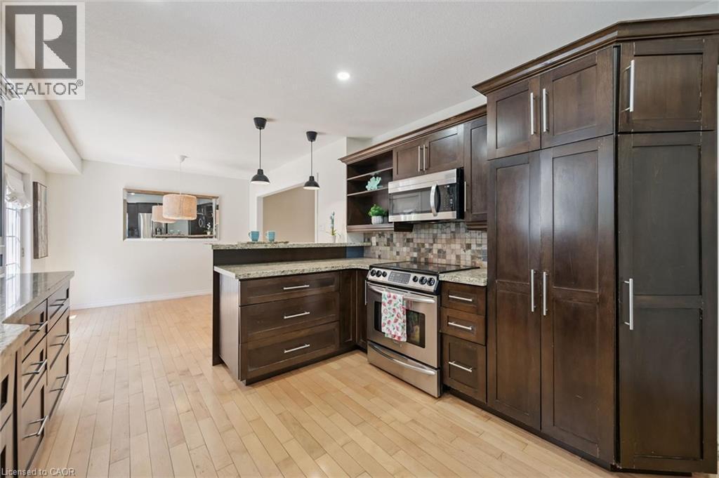 Gourmet kitchen featuring rich wood cabinetry with ample storage, stainless steel appliances including a professional-style range, quartz countertops, tile backsplash, and a substantial island with se - 345 Beechlawn Drive, Waterloo, ON