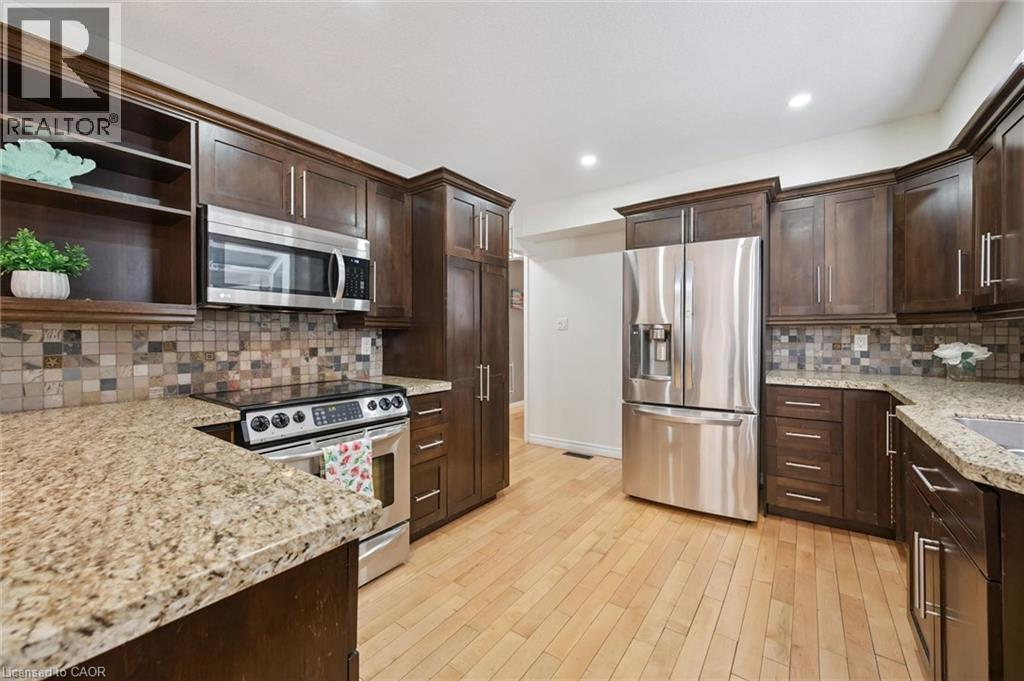 Kitchen featuring wood-finish cabinetry, stainless steel appliances, granite countertops, and a mosaic tile backsplash - 345 Beechlawn Drive, Waterloo, ON