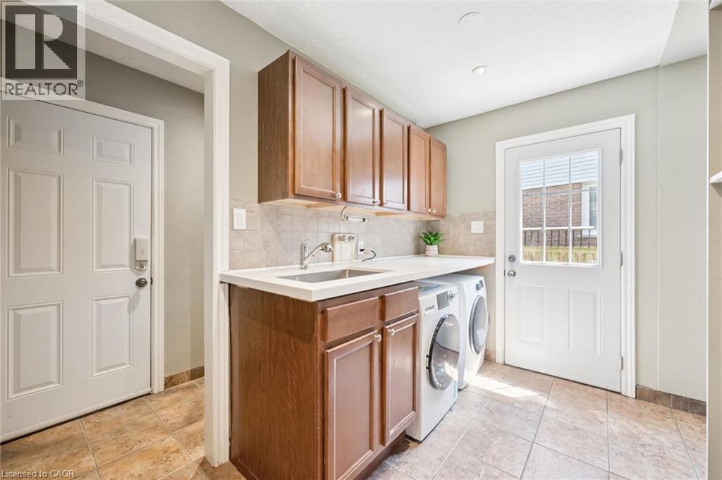 Laundry area featuring wood-finish cabinetry, a solid surface countertop with an integrated sink, a tiled backsplash, and ceramic tile flooring - 345 Beechlawn Drive, Waterloo, ON