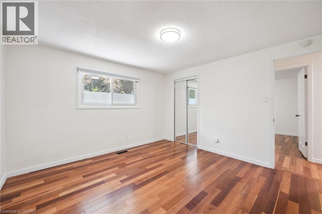 Bedroom featuring wood-finish flooring, a window with a roller blind, and mirrored closet doors - 345 Beechlawn Drive, Waterloo, ON