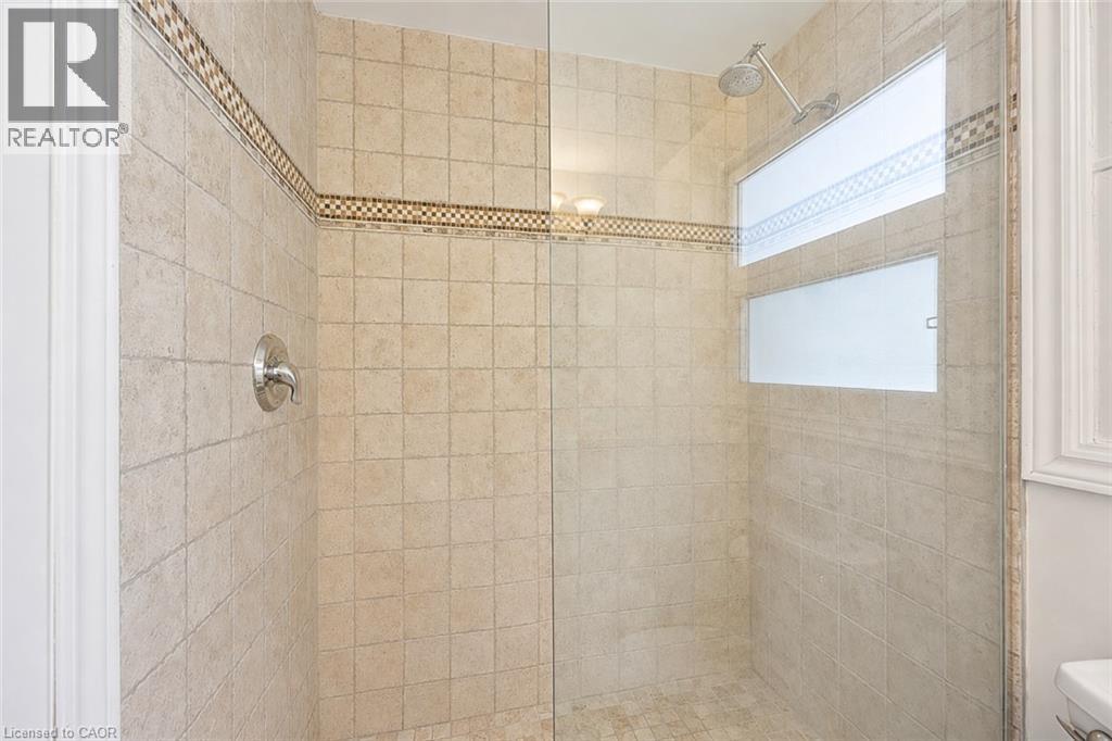 Glass-enclosed shower with full-height neutral-toned tile walls, decorative mosaic accent banding, and a rainfall showerhead - 345 Beechlawn Drive, Waterloo, ON