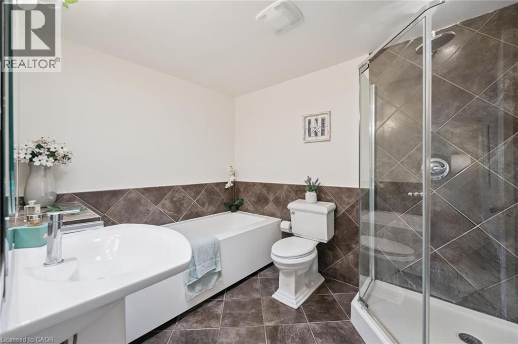 Full bathroom featuring a glass-enclosed shower, a separate bathtub, a white vanity with an integrated sink, and large format floor and wall tiles - 345 Beechlawn Drive, Waterloo, ON