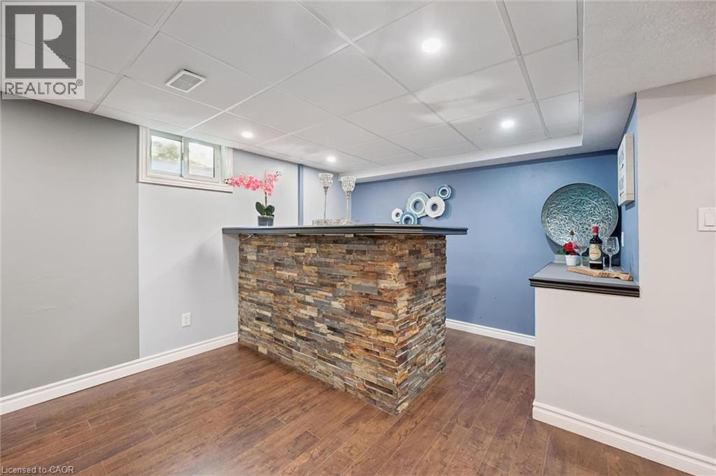 Finished basement featuring a striking brick-veneer bar with black countertop, wood-finish flooring, and fresh two-tone paint with blue accent wall - 345 Beechlawn Drive, Waterloo, ON