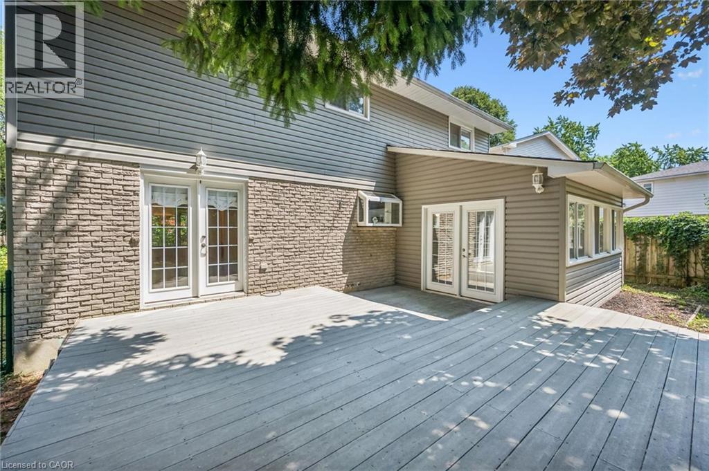 Expansive exterior deck offering multiple access points, featuring dual sets of white paneled French doors, grey horizontal siding, and a stone veneer foundation - 345 Beechlawn Drive, Waterloo, ON