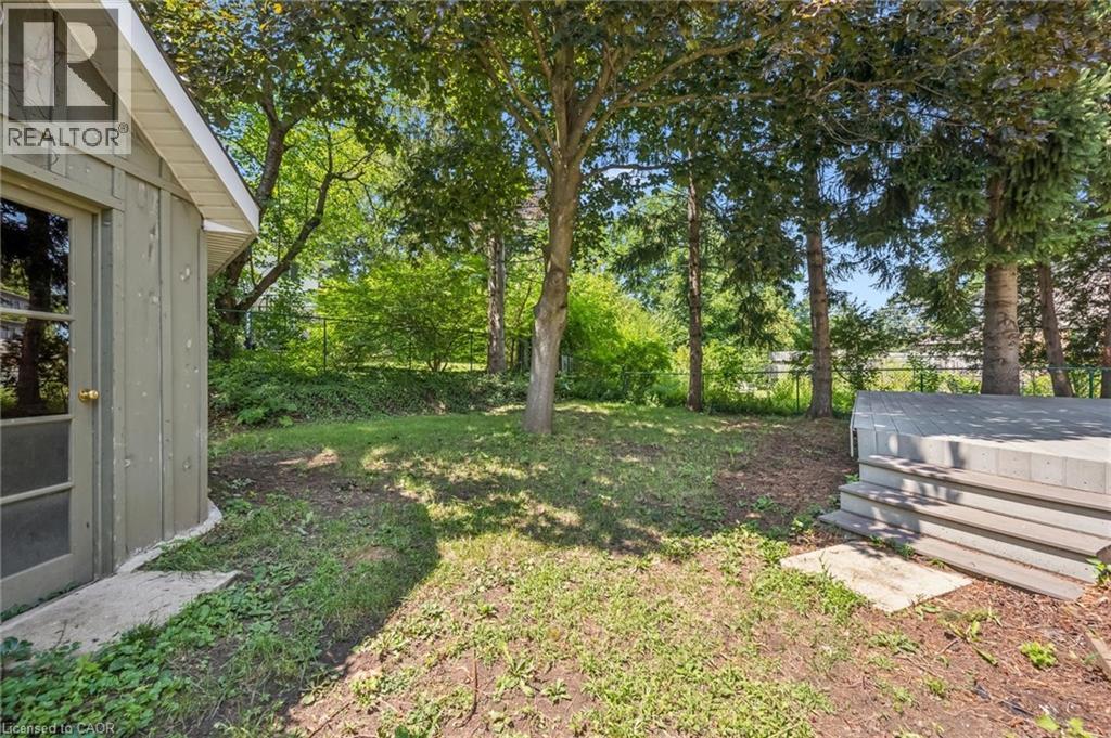 Expansive rear yard featuring mature trees, a concrete paver patio, and a storage structure with board and batten siding - 345 Beechlawn Drive, Waterloo, ON