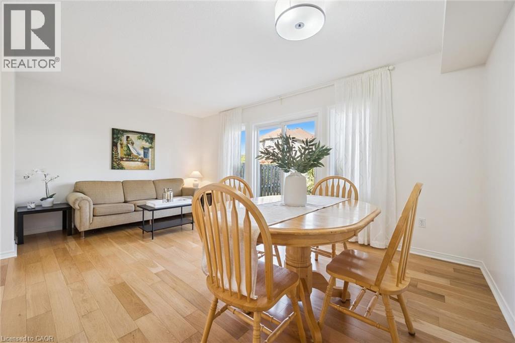 Open-concept living and dining area featuring wood-finish flooring, white walls, and a large sliding glass door - 151 Clairfields Drive Unit# 3, Guelph, ON