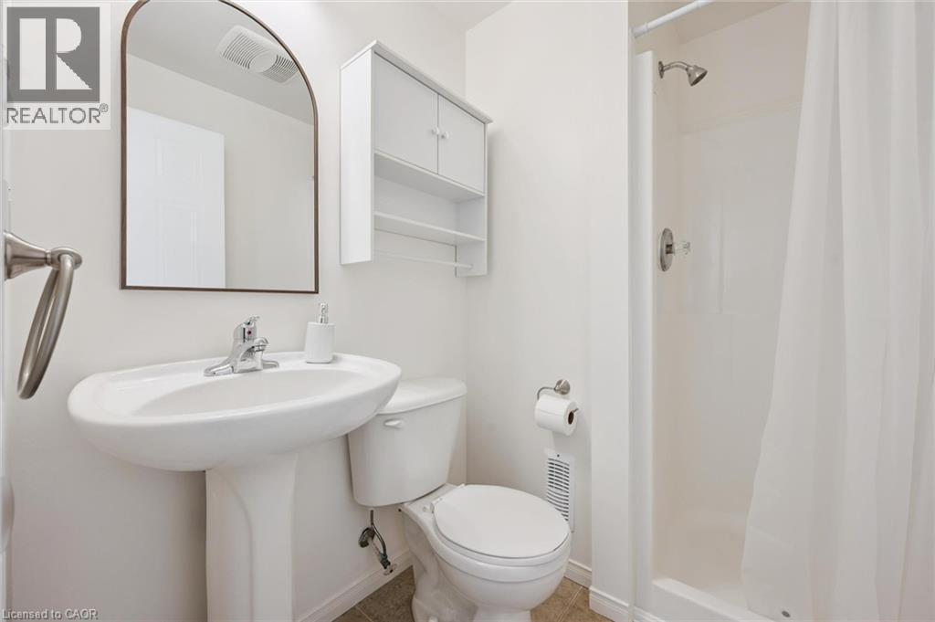 Pedestal sink with chrome fixtures, arched mirror, wall-mounted storage cabinet, and a shower with a white curtain - 151 Clairfields Drive Unit# 3, Guelph, ON