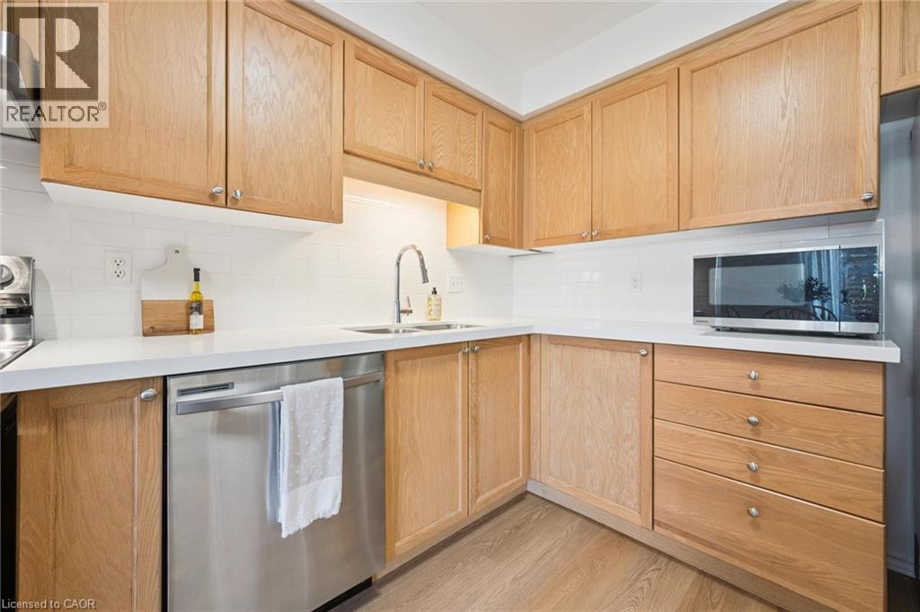 Wood-finish cabinetry, white subway tile backsplash, stainless steel dishwasher, and a stainless steel sink with a gooseneck faucet - 151 Clairfields Drive Unit# 3, Guelph, ON