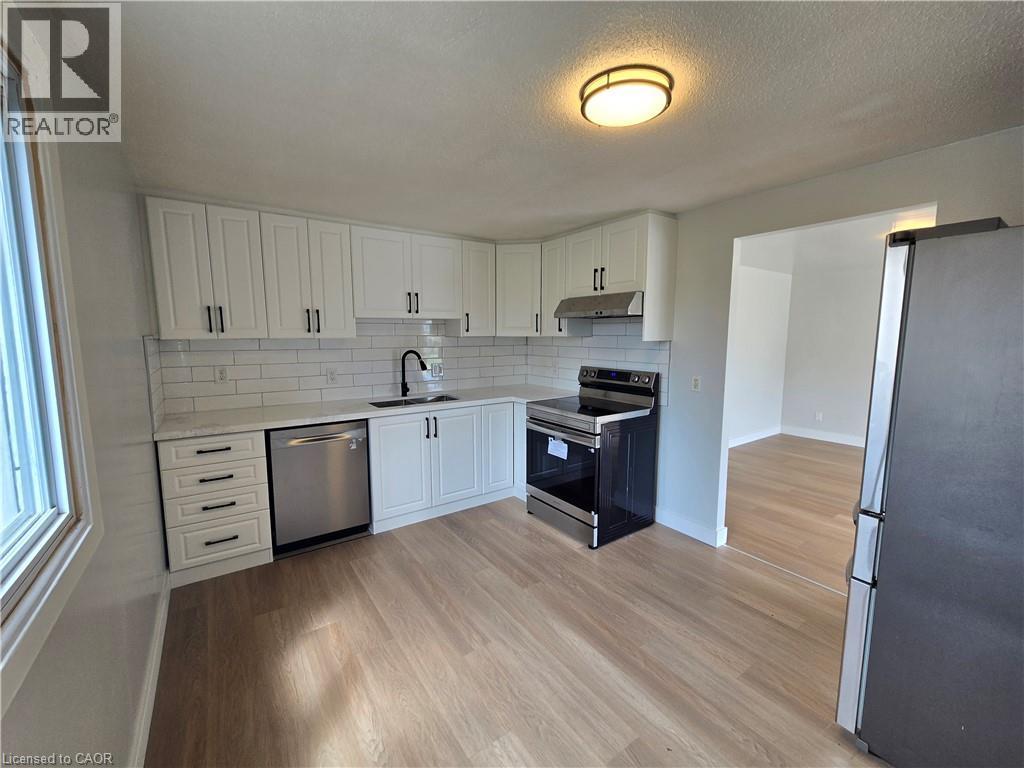 Kitchen featuring white shaker-style cabinetry, stainless steel appliances, a white subway tile backsplash, light-toned wood-finish flooring, and a contemporary flush-mount ceiling light - 99 Cluthe Crescent, Kitchener, ON