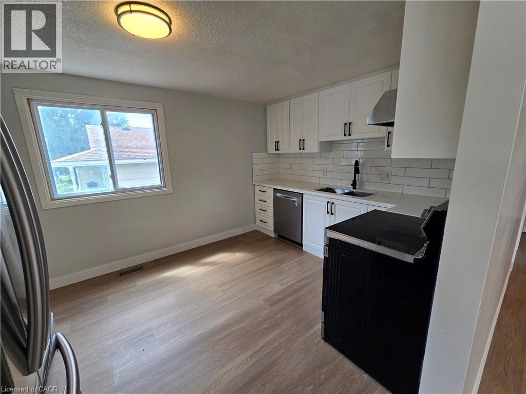 White shaker cabinetry, light-toned wood-finish flooring, white subway tile backsplash, stainless steel dishwasher, and a contemporary black faucet - 99 Cluthe Crescent, Kitchener, ON