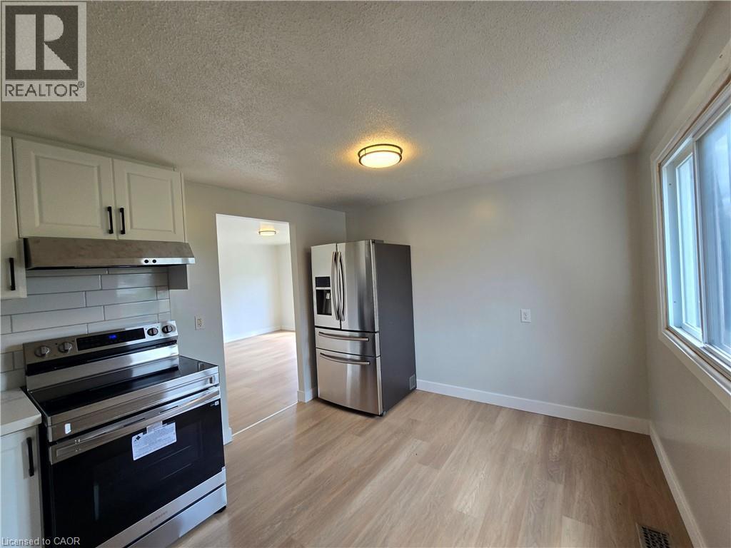 Kitchen featuring wood-finish flooring, white cabinetry with black hardware, stainless steel appliances, and a window - 99 Cluthe Crescent, Kitchener, ON