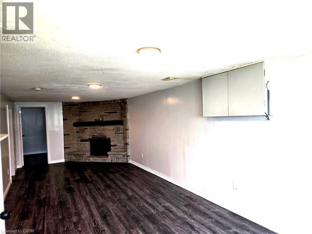 Stone-clad fireplace feature with a dark mantel, dark wood-finish flooring, and recessed ceiling lighting - 99 Cluthe Crescent, Kitchener, ON