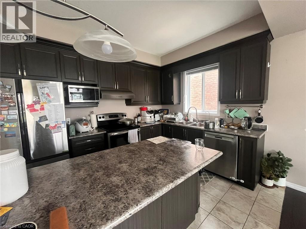 Kitchen featuring dark wood-finish cabinetry, stainless steel appliances, a center island with a speckled countertop, and tiled flooring - 298 Buttonbush Street, Waterloo, ON