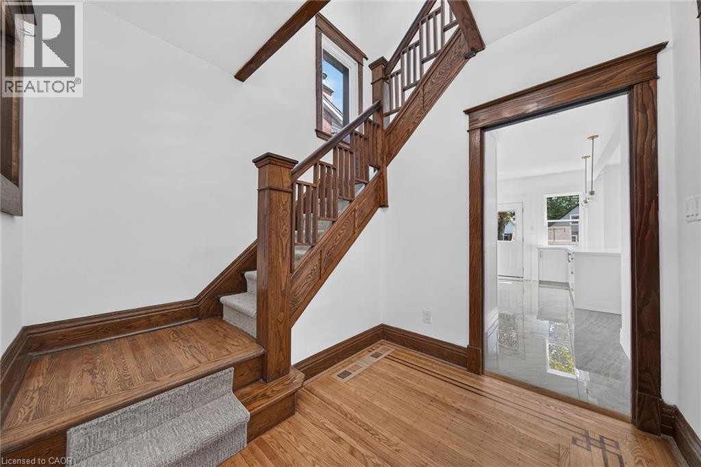 Solid wood staircase with carpeted treads, wood-finish flooring with decorative inlay, and a doorway with wood trim - 229 Park Row S, Hamilton, ON