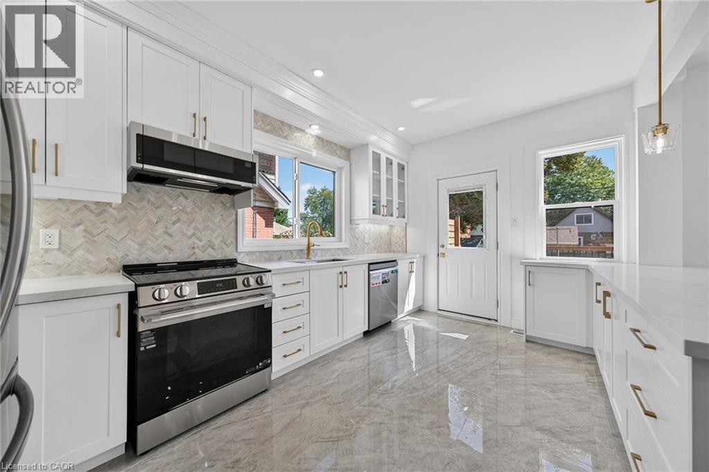 Modern kitchen featuring white cabinetry, stainless steel appliances, stone countertops, a herringbone tile backsplash, and polished floor tiles - 229 Park Row S, Hamilton, ON