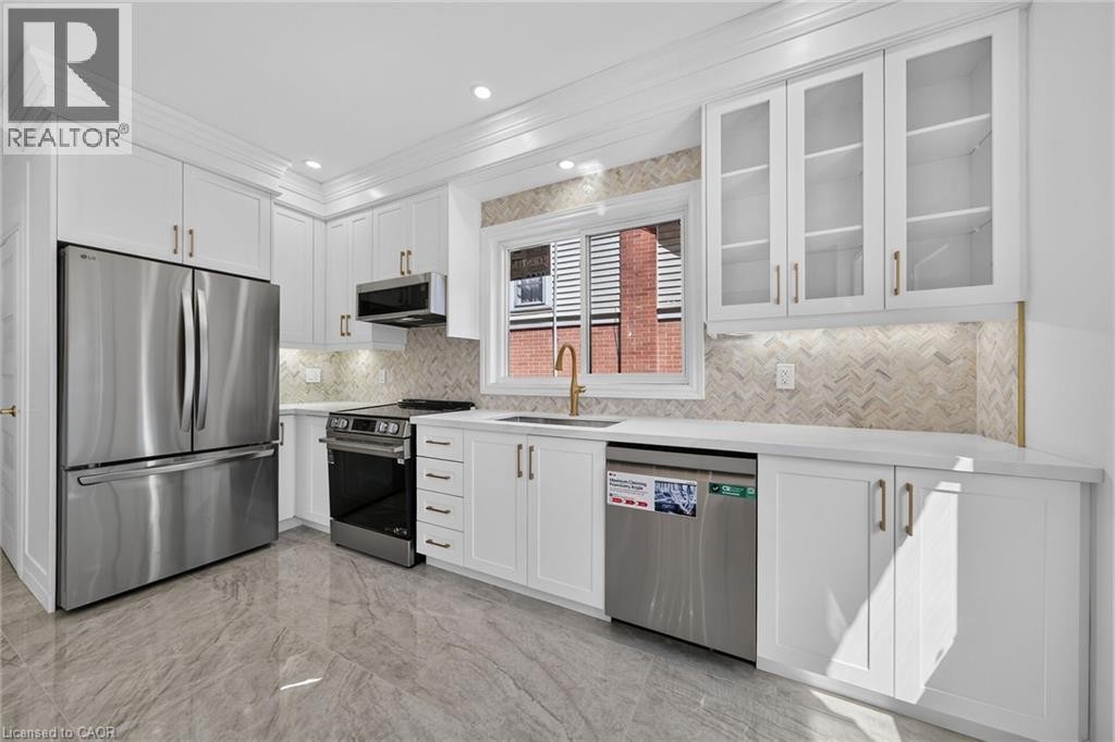 White cabinetry with gold-tone hardware, stainless steel appliances, a herringbone tile backsplash, recessed lighting, and wood-finish flooring - 229 Park Row S, Hamilton, ON