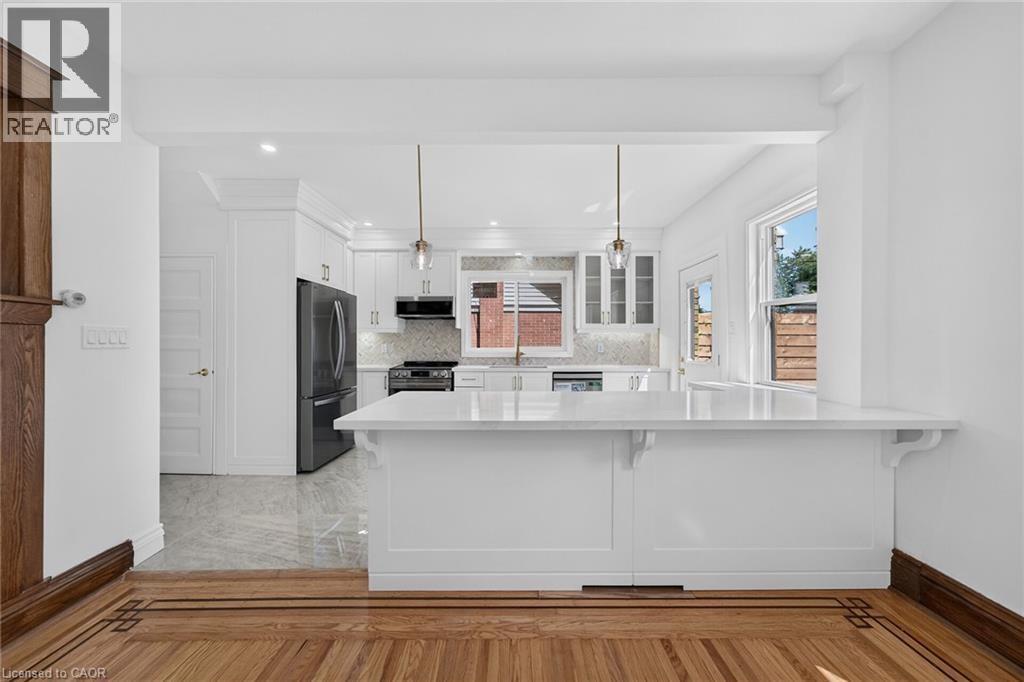 Renovated kitchen featuring white cabinetry, stainless steel appliances, and a central island with a breakfast bar - 229 Park Row S, Hamilton, ON