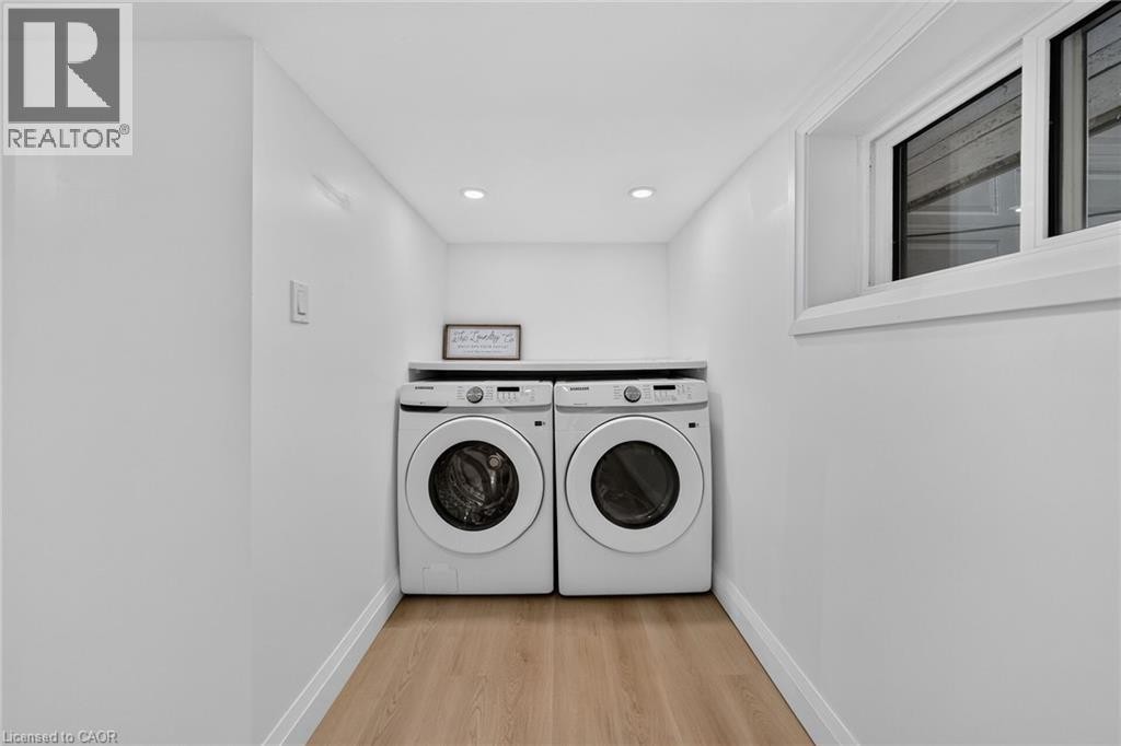 Dedicated laundry area featuring front-loading appliances, wood-finish flooring, and recessed lighting - 229 Park Row S, Hamilton, ON