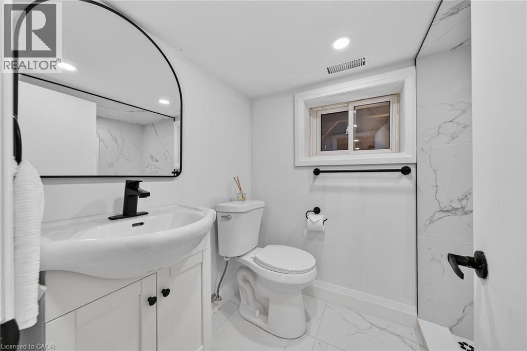 Modern bathroom featuring a curved black-framed mirror with integrated lighting, white ceramic vessel sink with matte black faucet and wall-mounted fixtures, marble-look tile flooring and wall surface - 229 Park Row S, Hamilton, ON