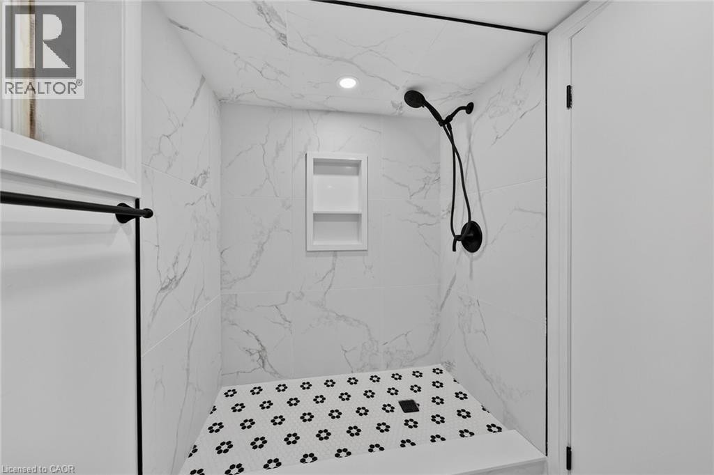 Walk-in shower with large format wall tiles, built-in recessed shelving, a black shower fixture, and a mosaic tile floor - 229 Park Row S, Hamilton, ON