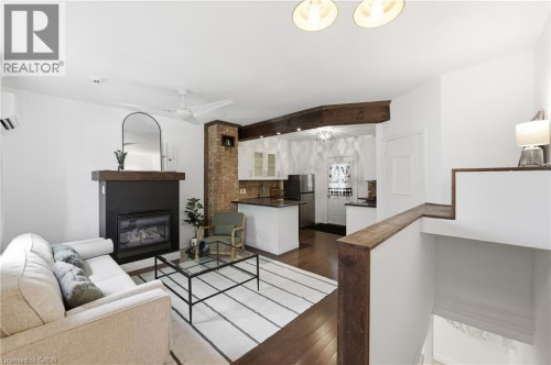 Open-concept living area featuring wood-finish flooring, a contemporary fireplace, and an exposed brick accent - 128 Robert Street, Hamilton, ON 