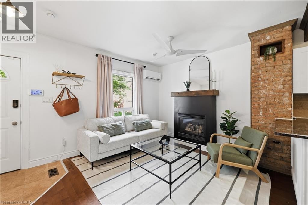 Gas fireplace with a wood mantle, exposed brick column, and ceiling fan - 128 Robert Street, Hamilton, ON