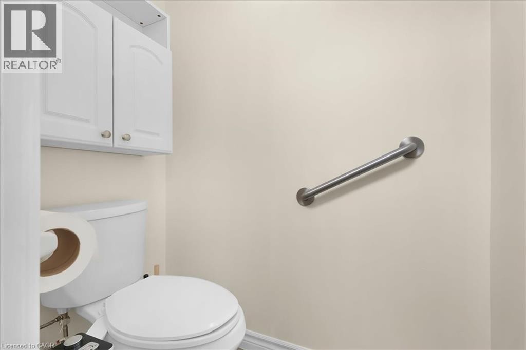 White wall cabinets with brushed nickel hardware, a white toilet, and a wall-mounted metal grab bar - 150 Bankside Drive, Kitchener, ON
