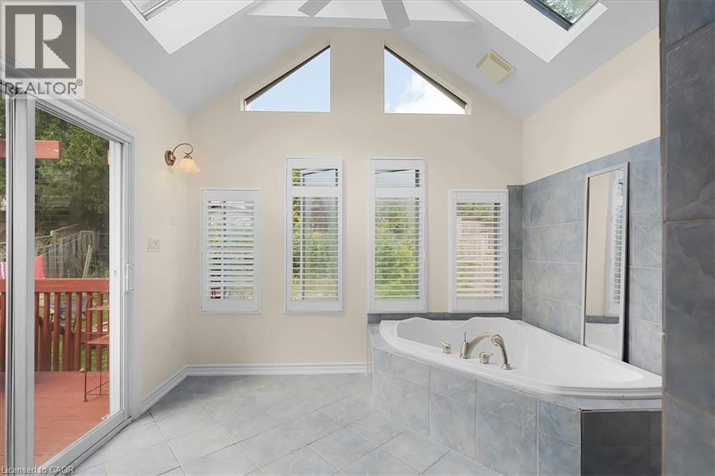 Vaulted ceiling with skylights, built-in soaking tub, sliding glass door to a private deck, and tiled flooring - 150 Bankside Drive, Kitchener, ON