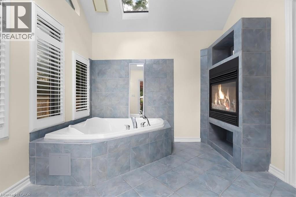 Vaulted ceiling with skylight, tile-surround corner soaking tub, integrated fireplace, and tile flooring - 150 Bankside Drive, Kitchener, ON