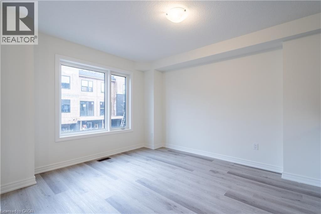 Spacious interior featuring wood-finish flooring, neutral paint, a large double window, and a flush mount ceiling light - 23 Dryden Lane, Hamilton, ON