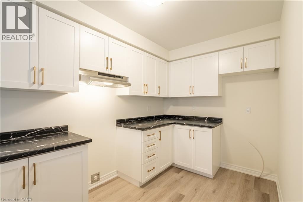 Modern kitchen featuring white cabinetry with brushed gold hardware, black countertops with waterfall edge detailing, stainless steel range hood, and wood-finish flooring throughout - 23 Dryden Lane, Hamilton, ON