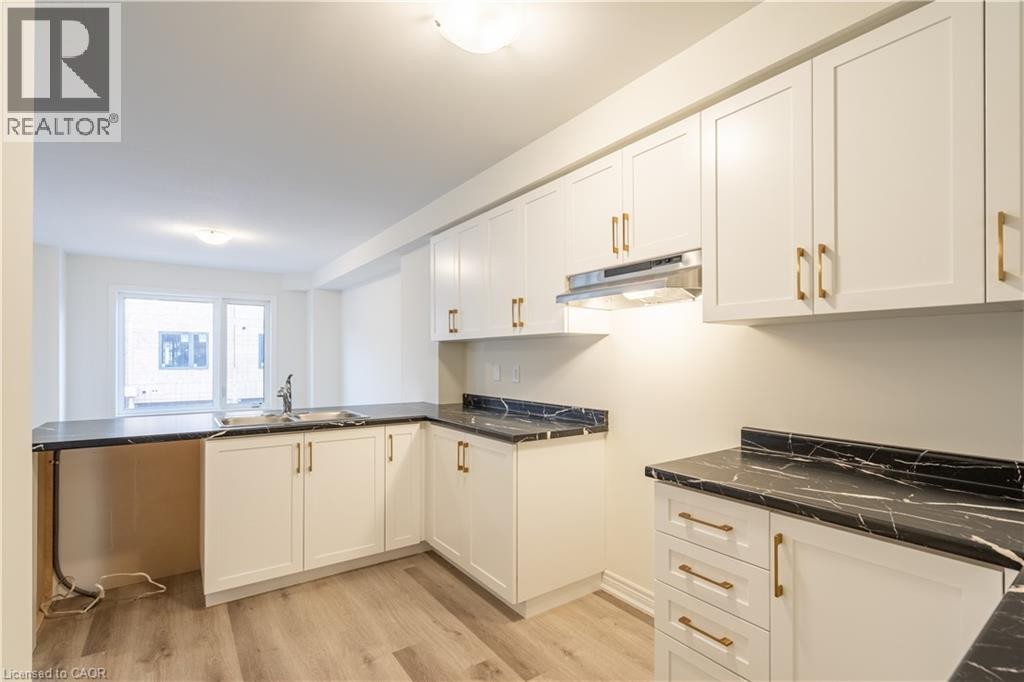 Kitchen featuring white cabinetry, gold-finish hardware, dark marble-look countertops, and wood-finish flooring - 23 Dryden Lane, Hamilton, ON